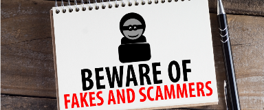 Notepad with the words "beware of fakes and scammers" sitting on a table with a pen