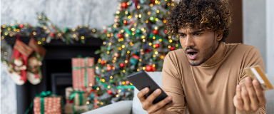 Man looking at phone in surprise in front of a Christmas tree