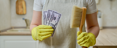 Woman in rubber gloves holding money and a cleaning brush