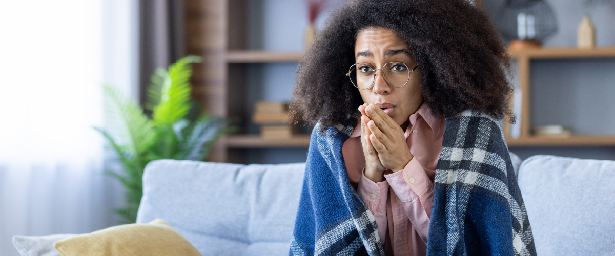 Cold woman rubbing her hands together with a blanket wrapped around her shoulders