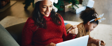 Woman in holiday sweater shopping on her laptop with daughter in background