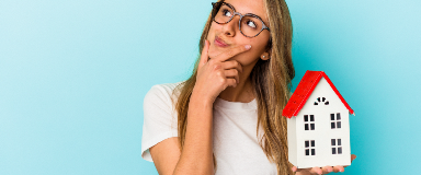 Young woman looking thoughtful holding a small house.
