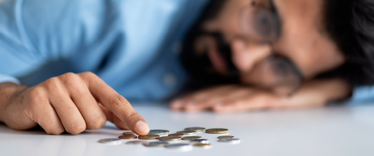 Man sadly laying his head on a table and counting coins