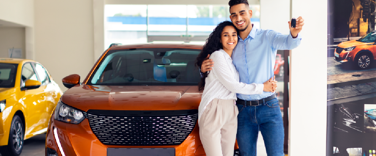 A couple holding the keys of their new car, standing in front of the car