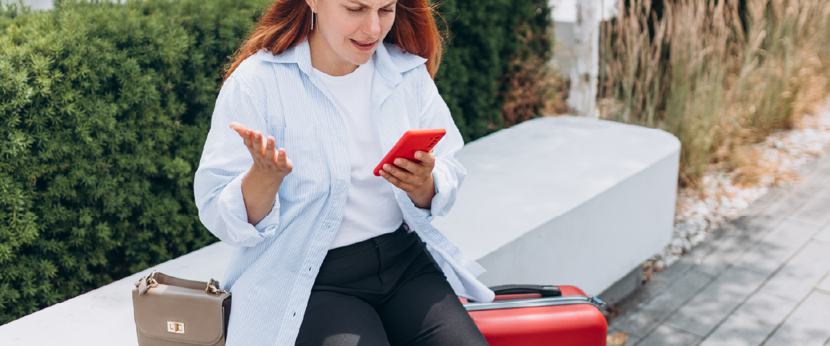 Frustrated woman with suitcase looking at her phone.