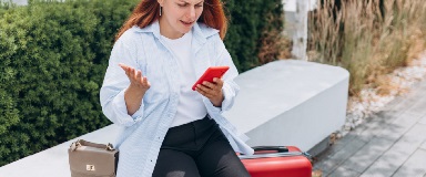 Frustrated woman with suitcase looking at her phone.