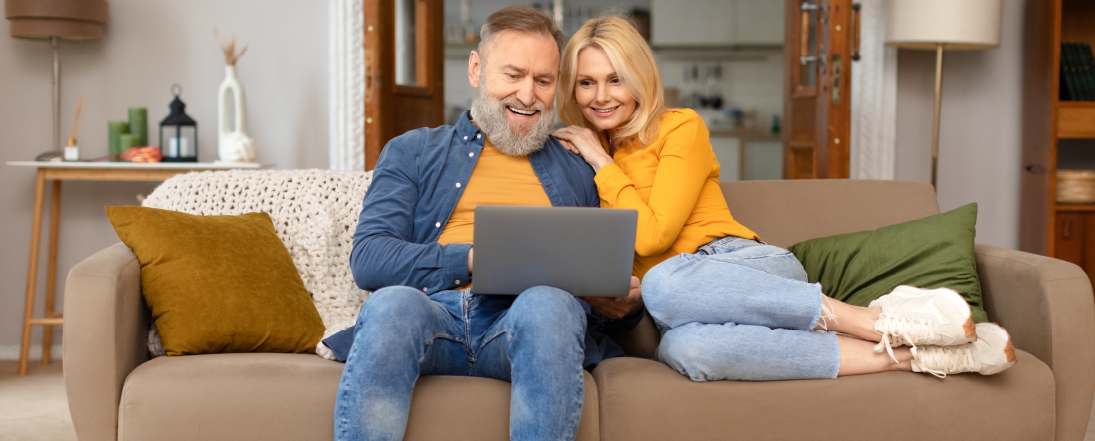 Smiling couple sitting on a couch and looking at a laptop together