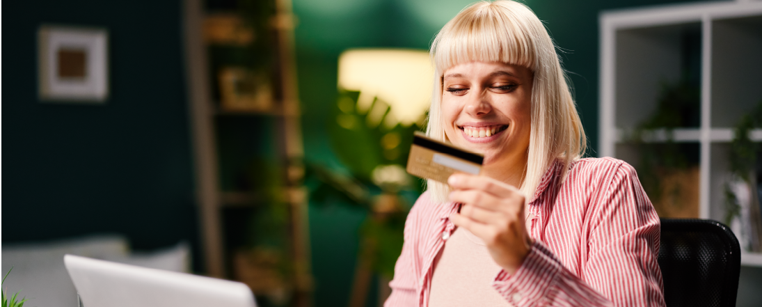 Young woman holding a debit card and smiling while online shopping