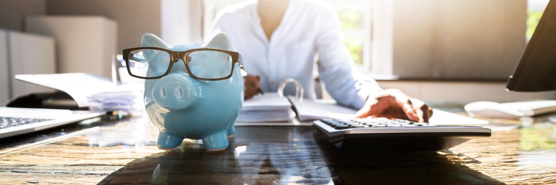 Piggy bank with glasses on it and person calculating in the background