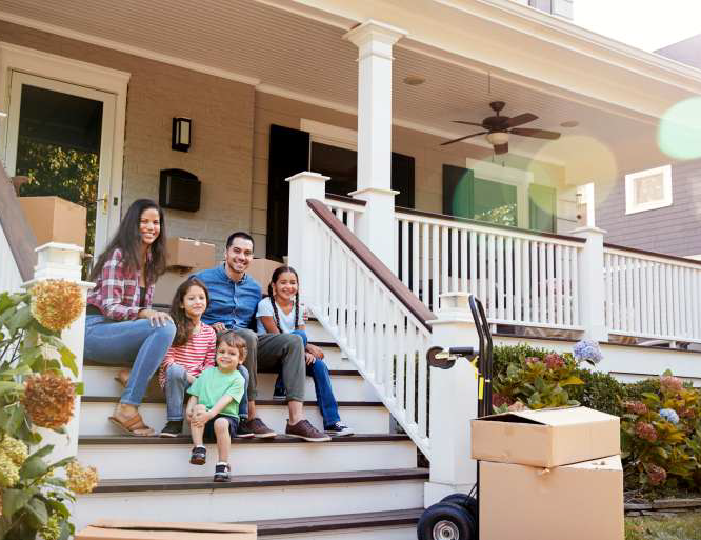 Family sitting on front porch of new house surrounded by moving boxes