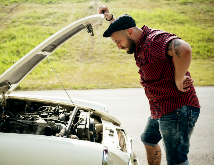 Man looking under the hood of his broken down car