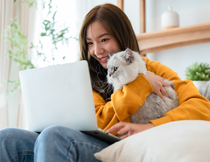 Woman looking at her laptop while cuddling her cat