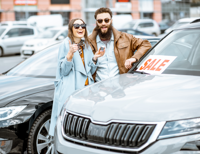Young couple celebrating behind car